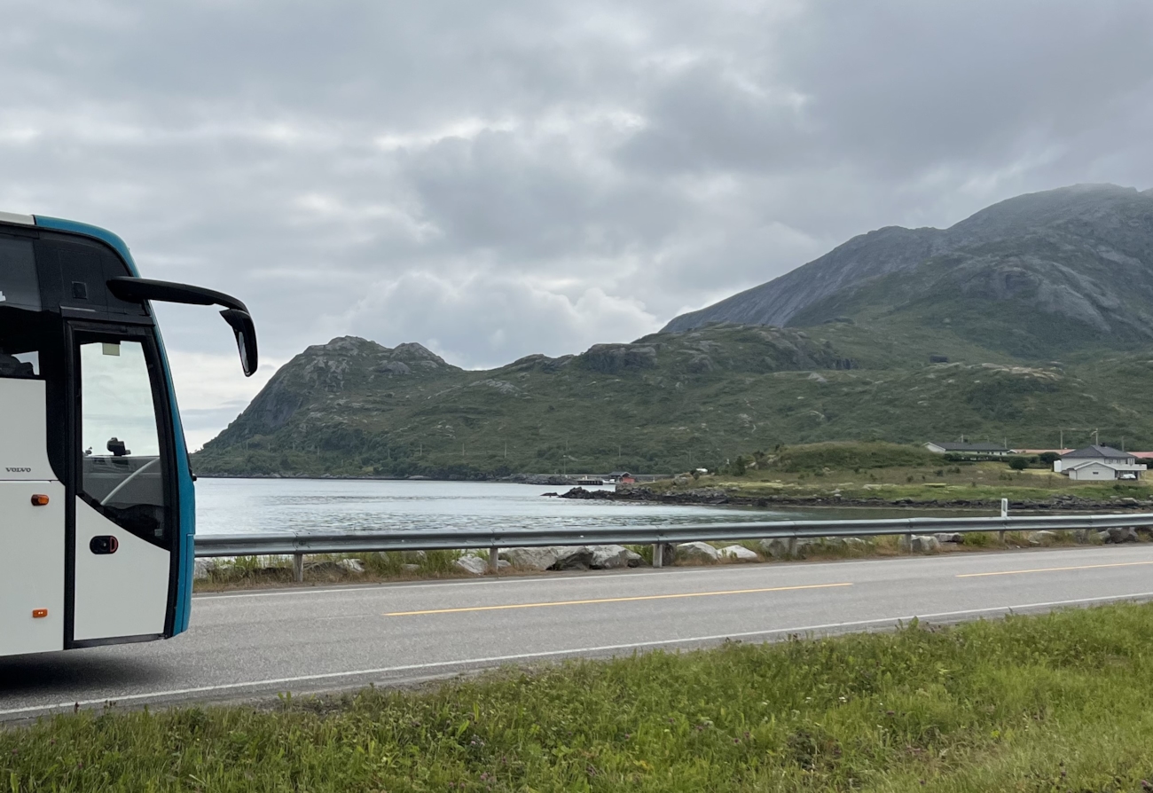 Bildet viser en buss med vann og fjell i bakgrunn